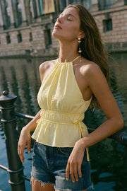 Top corto de cuello halter con plisados, tirantes delgados, detalle de rib con plisados y lazos laterales en costados, peplum con olanes en bajo y cierre posterior con botón y ojal.