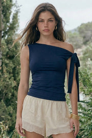 Top asimétrico de fit ajustado, sin mangas, escote diagonal, hombro descubierto y detalle decorativo de nudo amarrable.
