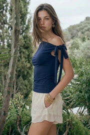 Top asimétrico de fit ajustado, sin mangas, escote diagonal, hombro descubierto y detalle decorativo de nudo amarrable.