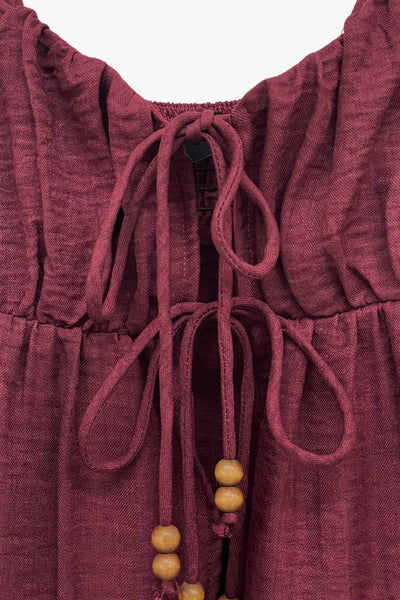 Top de lino, tirantes delgados ajustables, corte en a, capas con olanes en bajo, escote v redondeado con plisados y cut out, abertura frontal y cierre con lazos amarrables. Detalle de fruncido en espalda y detalle decorativo en lazos.