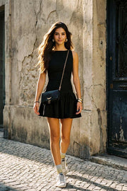 Vestido corto de fit ajustado, cuello redondo, sin mangas, corte en a, plisados en cadera con lazos decorativos frontales y olanes en bajo. Cierre posterior con cremallera visible en contraste.