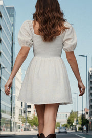 Vestido corto bordado, de talle fruncido, escote v, manga corta abullonada con rib elástico en bordes y corte en a con olanes en bajo.