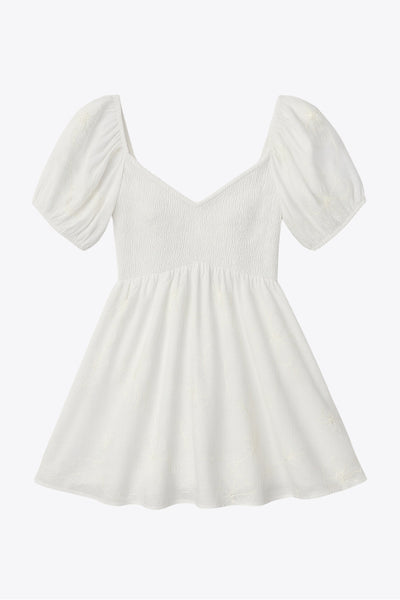 Vestido corto bordado, de talle fruncido, escote v, manga corta abullonada con rib elástico en bordes y corte en a con olanes en bajo.