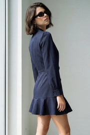 Vestido corto cruzado tipo blazer, fit ajustado, de manga larga abullonada con puño abotonado, solapa, doble cruce de botones y bajo con olanes en borde.
