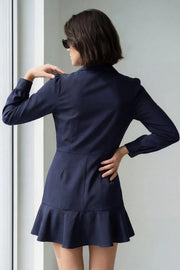 Vestido corto cruzado tipo blazer, fit ajustado, de manga larga abullonada con puño abotonado, solapa, doble cruce de botones y bajo con olanes en borde.