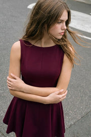 Vestido corto de cuello barco, sin mangas, cortes frontales, escote en espalda y corte en a con olanes en bajo.
