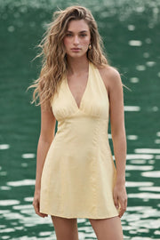 Vestido corto de cuello halter con lazo amarrable posterior, sin mangas, escote v con cortes y plisados frontales, corte en a, cortes frontales y escote en espalda. Cierre posterior con cremallera oculta.