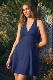 Vestido corto de cuello halter con lazo amarravle posterior, sin mangas, escote v con cortes y plisados frontales, corte en a, cortes frontales y escote en espalda. Cierre posterior con cremallera oculta.