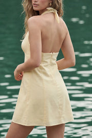 Vestido corto de cuello halter con lazo amarrable posterior, sin mangas, escote v con cortes y plisados frontales, corte en a, cortes frontales y escote en espalda. Cierre posterior con cremallera oculta.