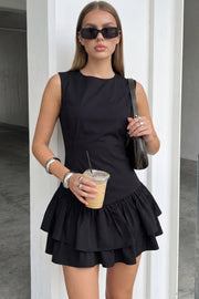 Vestido corto de fit ajustado, sin mangas, cuello redondo, pinzas frontales, plisados en cadera y corte en a con capas de olanes en bajo. Cierre posterior con cremallera oculta.