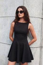 Vestido corto de corte en a, cuello barco, sin mangas, pinzas frontales con cortes y olanes en bajo. Detalle de escote en espalda.