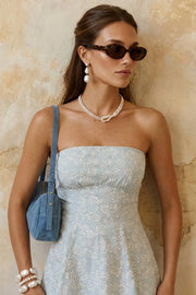 Vestido corto strapless, estampado, de fit ajustado, escote recto, corte frontal con plisados, corte en a y olanes en bajo. Detalle de cut out en espalda con nudo amarrable y cierre con cremallera visible en contraste.