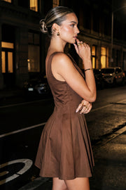 Vestido corto de fit ajustado, cuello barco, sin mangas, pinzas frontales, corte en a y olanes en bajo.