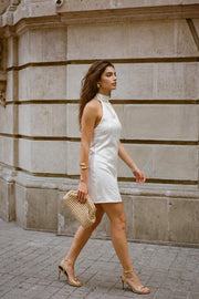 Vestido corto satinado de fit ajustado, cuello halter alto con plisados decorativos, sin mangas, escote en espalda, cierre posterior con botón, ojal y cremallera oculta.