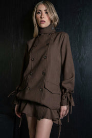 Vestido corto de fit recto, con hombreras, manga larga amplia con jareta y olanes en puños, pinza de amplitud en espalda, bolsillos delanteros con cartera, jareta laterales en bajo con olanes en borde y cierre frontal con doble cruce de botones en contraste. Detalle de cuello alto con trabilla y botón decorativos.