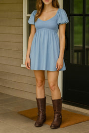 Vestido corto de lino, talle fruncido, escote v, manga corta abullonada con rib elástico en bordes y corte en a con olanes en bajo.