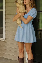 Vestido corto de lino, talle fruncido, escote v, manga corta abullonada con rib elástico en bordes y corte en a con olanes en bajo.