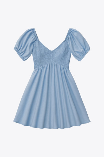 Vestido corto de lino, talle fruncido, escote v, manga corta abullonada con rib elástico en bordes y corte en a con olanes en bajo.