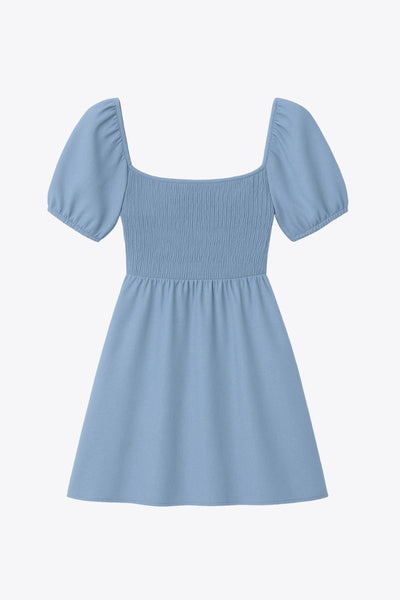 Vestido corto de lino, talle fruncido, escote v, manga corta abullonada con rib elástico en bordes y corte en a con olanes en bajo.