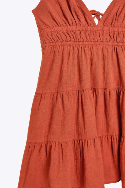 Vestido corto de escote v, corte en a con capas de olanes en bajo, rib elástico en cintura, tirantes delgados con lazado ajustable posterior y escote en espalda.