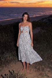 Vestido midi strapless de estampado floral, escote corazón con nudo amarrable, cut out frontal, cintura elástica, detalle de capas de olanes en bajo y fruncido en espalda.