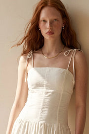 Vestido largo de fit ajustado, corte en a con olanes, plisados en cadera, tirantes delgados con nudo amarrable, escote recto y cierre posterior con cremallera oculta.