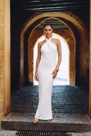 Vestido largo de fit fluido, cuello halter cruzado con lazo amarrable posterior, escote en espalda y cierre posterior con cremallera oculta. Detalle de abertura lateral en bajo.