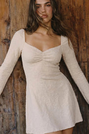 Vestido corto de escote corazón con cortes y plisados decorativos frontales, rib elástico en hombros, manga larga con puño amplio y corte en a. Detalle de textura en tejido y rib rizado en bajo.