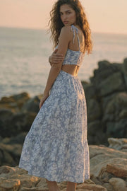 Vestido largo de corte en a, estampado floral, tirantes delgados con nudo amarrable, bajo con capas de olanes, cut out en costados y espalda. Detalle de rib elástico en cintura y fruncido en espalda.