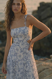 Vestido largo de corte en a, estampado floral, tirantes delgados con nudo amarrable, bajo con capas de olanes, cut out en costados y espalda. Detalle de rib elástico en cintura y fruncido en espalda.