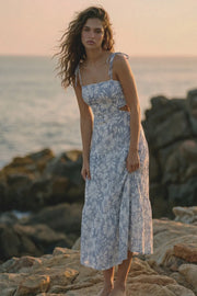 Vestido largo de corte en a, estampado floral, tirantes delgados con nudo amarrable, bajo con capas de olanes, cut out en costados y espalda. Detalle de rib elástico en cintura y fruncido en espalda.