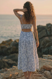 Vestido largo de corte en a, estampado floral, tirantes delgados con nudo amarrable, bajo con capas de olanes, cut out en costados y espalda. Detalle de rib elástico en cintura y fruncido en espalda.