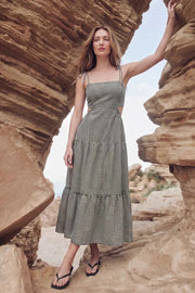Vestido largo de corte en a, estampado cuadros, tirantes delgados con nudo amarrable, bajo con capas de olanes, cut out en costados y espalda. Detalle de rib elástico en cintura y fruncido en espalda.
