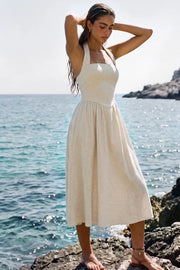 Vestido midi de lino, cuello halter con rib elástico, sin mangas, escote recto, cortes frontales, detalle frontal v en cintura con plisados y fruncido en espalda.