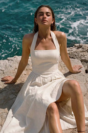 Vestido midi de lino, cuello halter con rib elástico, sin mangas, escote recto, cortes frontales, detalle frontal v en cintura con plisados y fruncido en espalda.