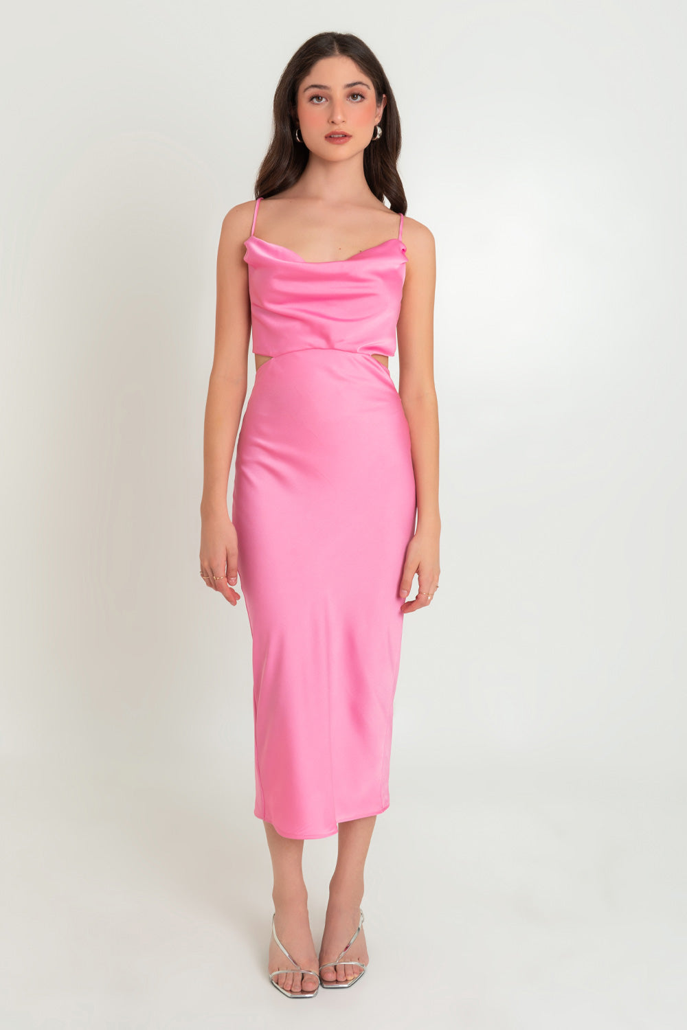 Woman in a pink satin midi dress standing against a white background.