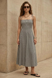 Vestido midi de estampado cuadros, tirantes delgados con nudo amarrable, escote recto, pinzas frontales y corte en a con olanes en bajo. Cierre posterior con cremallera oculta.