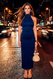 Vestido midi de fit ajustado, cuello alto halter, sin mangas, plisados en costados y abertura lateral en bajo. Cierre posterior con botones y ojales.