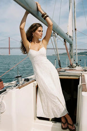 Maxi vestido bordado de corte en a con olanes en bajo, tirantes delgados con nudo amarrables, escote corazón con cortes y detalles plisados. Cierre posterior con cremallera visible en contraste y detalle de perforado en tejido.