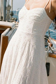 Maxi vestido bordado de corte en a con olanes en bajo, tirantes delgados con nudo amarrables, escote corazón con cortes y detalles plisados. Cierre posterior con cremallera visible en contraste y detalle de perforado en tejido.
