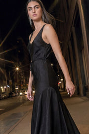 Vestido largo satinado de fit fluido, sin mangas, escote v, cortes decorativos en talle, escote fluido posterior y lazo decorativo amarrable en cintura. Cierre lateral con cremallera oculta.