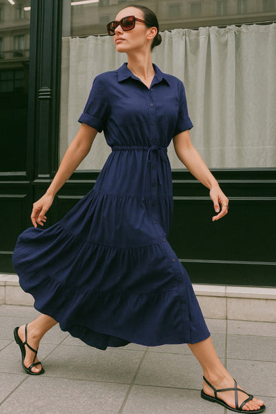 Maxi vestido camisero de manga corta con doblez en borde, cuello camisero, plisados frontales, olanes en bajo, jareta ajustable en cintura y cierre frontal con hilera de botones.