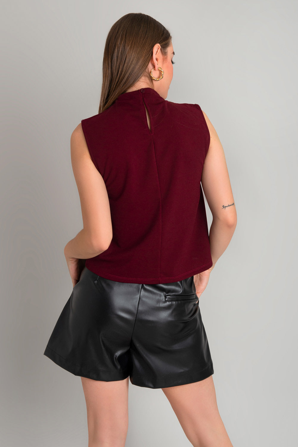 Blusa sin mangas de fit recto, cuello mock con detalles plisados y cierre posterior con botón y ojal.