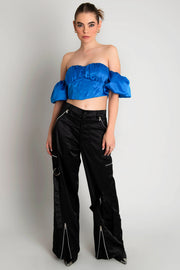 Top corset satinado de escote con detalles plisados, costuras frontales, bajo v frontal, hombros descubiertos y manga corta abullonada con olanes. Cierre con cremallera visible en contraste. 